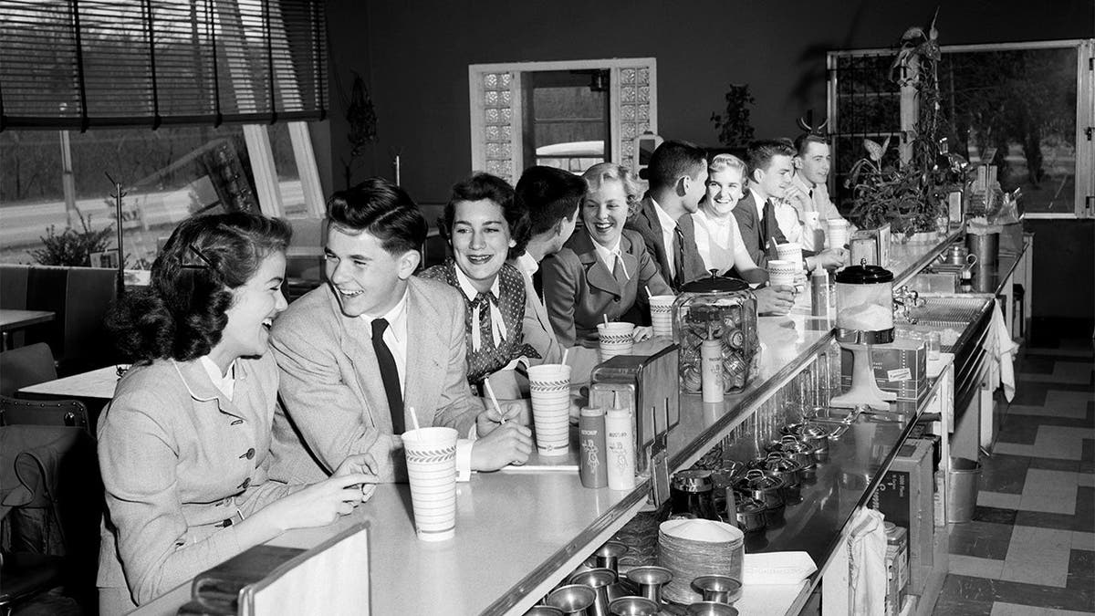 A group of young people sits at a lunch counter in the 1950s.