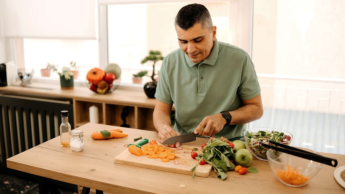 Young man chops vegetables in a home kitchen.