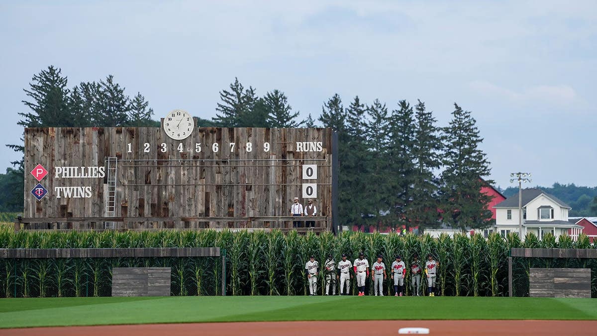 Minnesota Twins and Philadelphia Phillies players emerge from corn in the outfield.