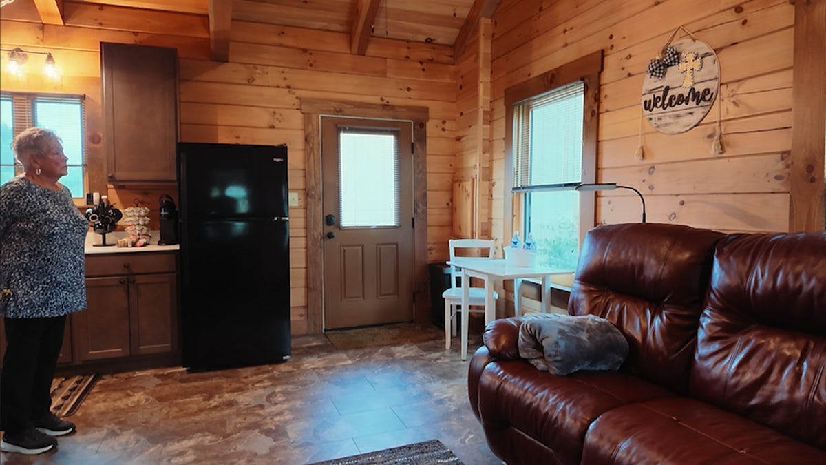 Wood-paneled cabin interior with a kitchenette, refrigerator, dining table and leather couch.