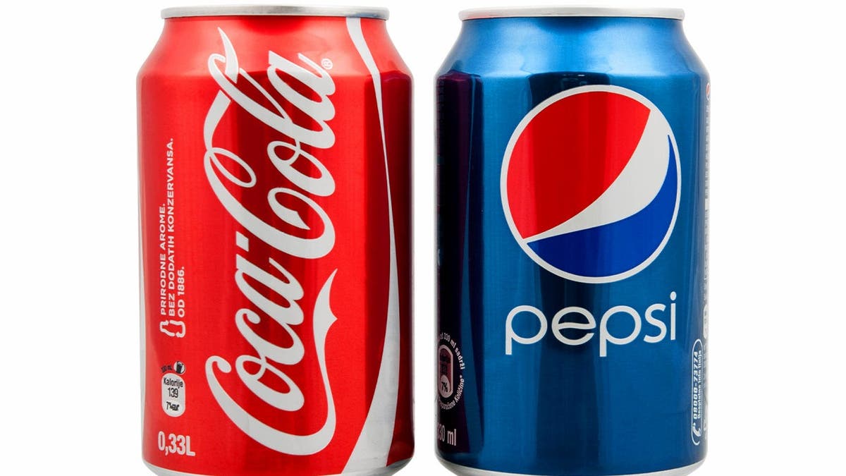 A can of Coke sits beside a can of Pepsi.