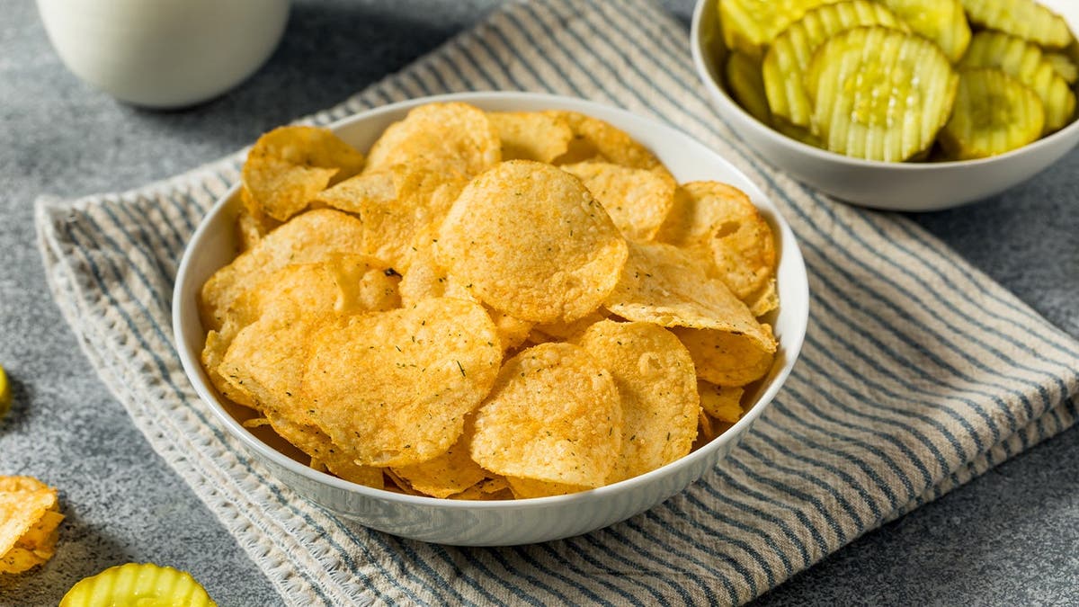 A bowl of pickle chips sits on a table.