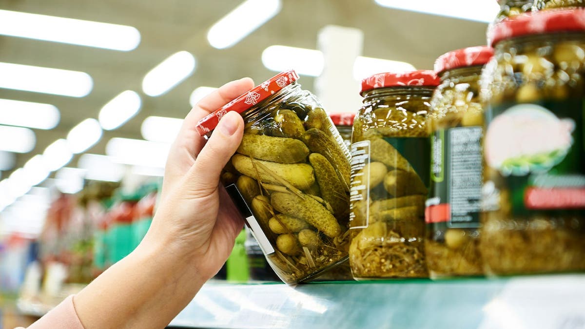 A person takes a jar of pickles off a store shelf.