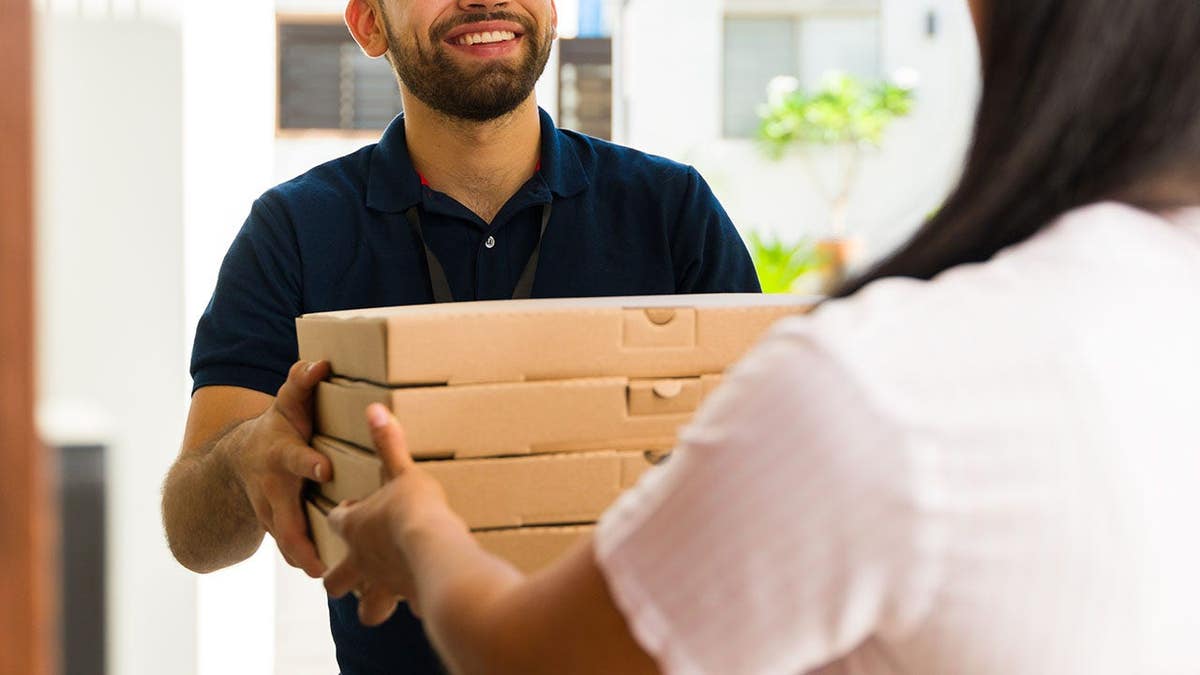 Pizza delivery man hands food order to woman at front door.
