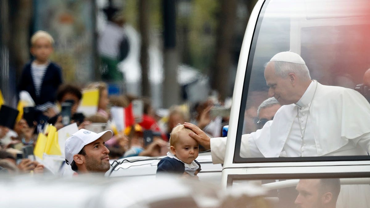 Pope Leo XIV waves from the popemobile on the Champs-Élysées in Paris.