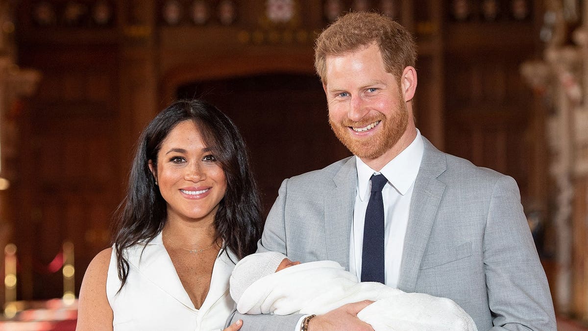Prince Harry and Meghan pose with their newborn son Archie in St George's Hall at Windsor Castle.