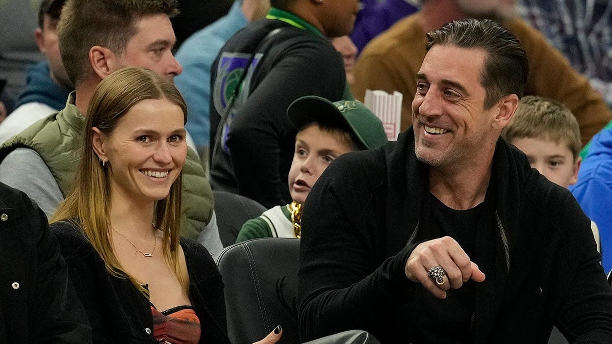 Randall Cobb, Mallory Edens and Aaron Rodgers seated watching a basketball game.