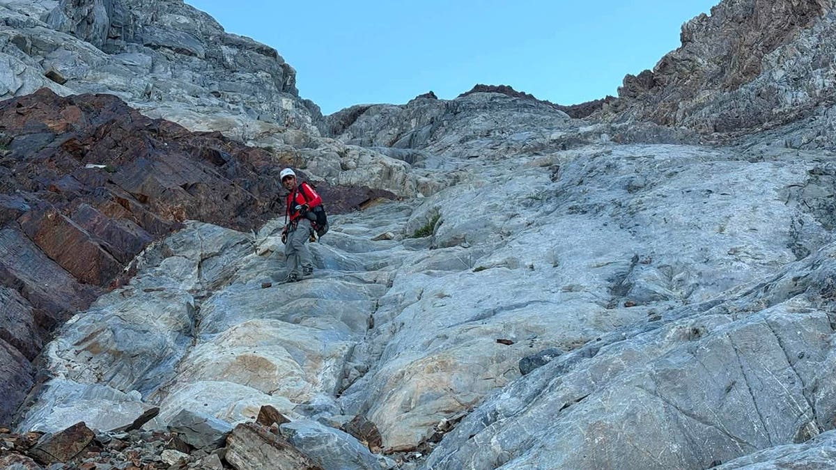 A rescuer going up the mountain to save a man stranded on a ledge.
