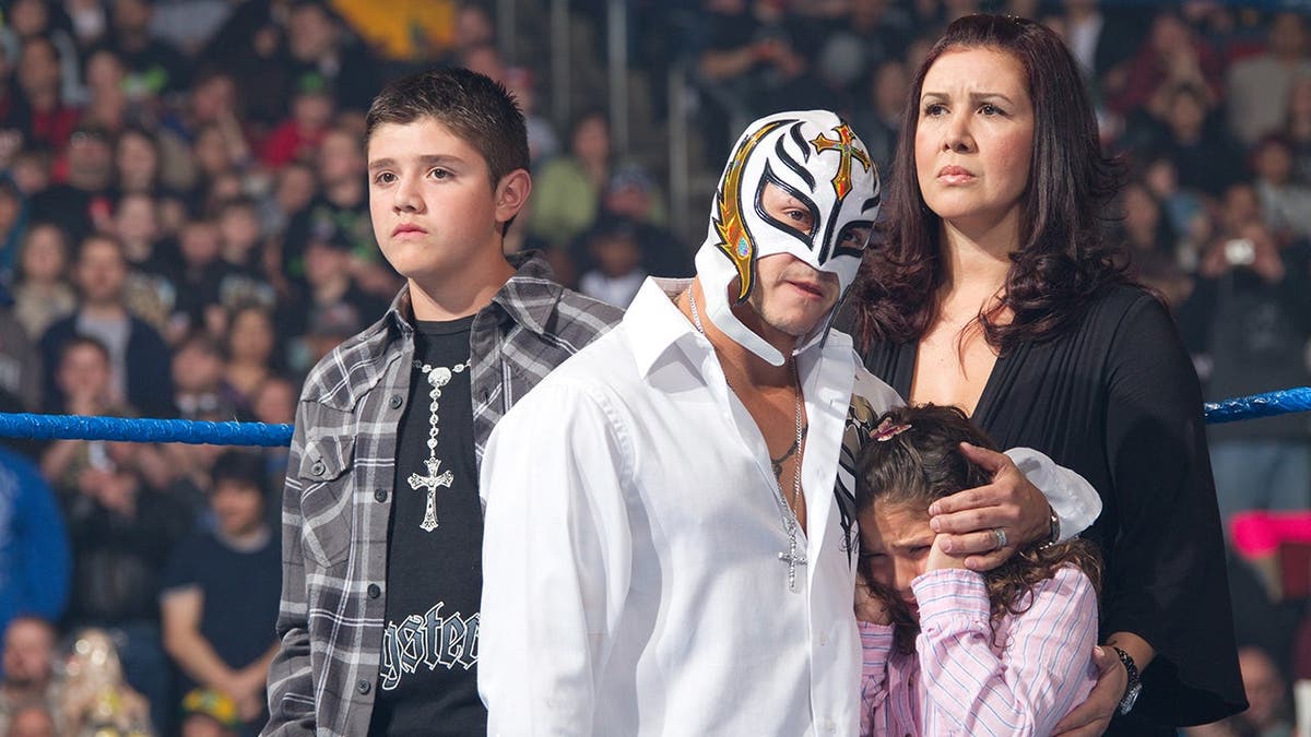 Rey Mysterio stands in the ring with Dominik Mysterio, Angie Gutierrez and Aaliyah Gutierrez.