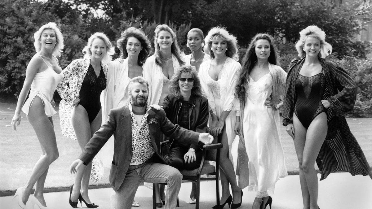 Ringo Starr stands with six women modeling swimwear and lingerie at a charity fashion show.