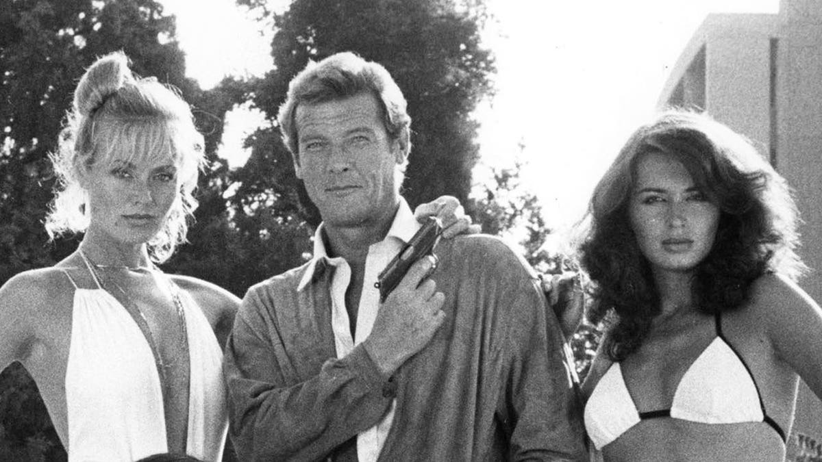 Roger Moore poses with six women in formal attire.
