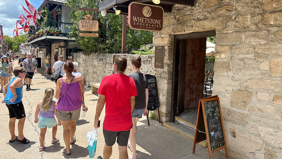 People walk by a sign for the Spanish Bakery & Cafe in St. Augustine, Florida.