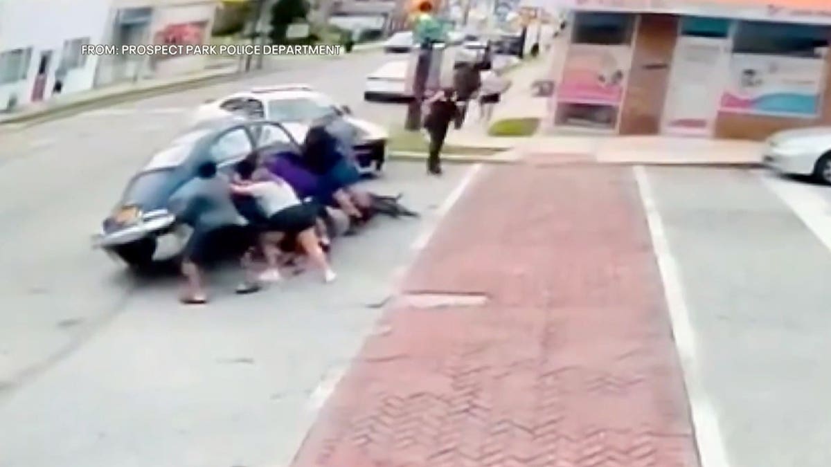 About six bystanders joined police officers to lift a Volkswagen Beetle and free a woman trapped underneath