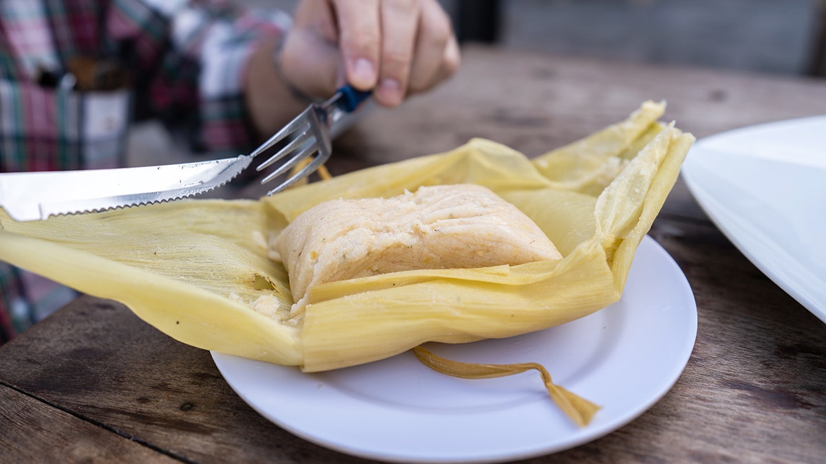 A man uses a fork and knife to eat a tamale.
