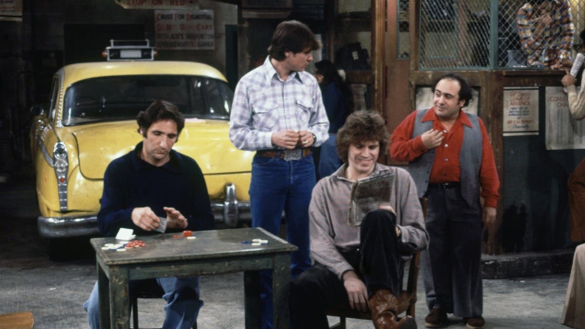 Judd Hirsch, Randall Carver, Jeff Conaway and Danny DeVito stand together in a taxicab office scene.