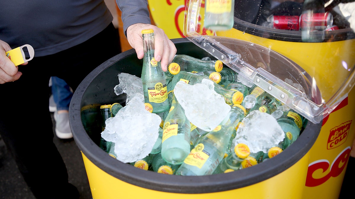 A man's hand removes a Topo Chico mineral water from a cooler designed to look like the drink.