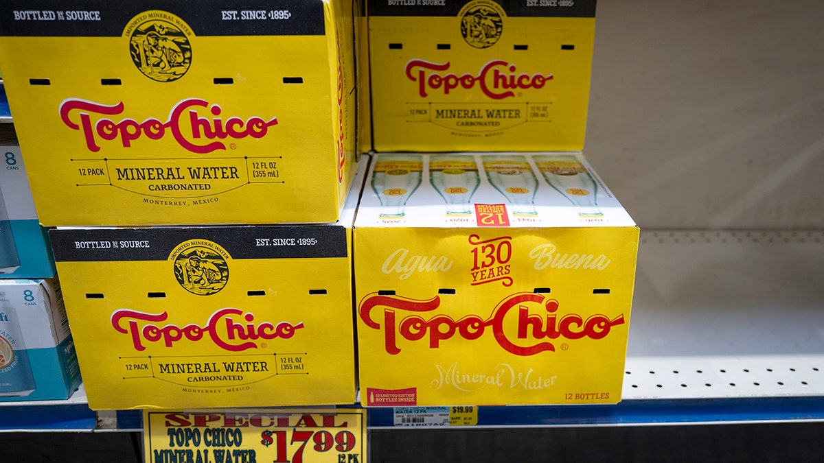 Four Topo Chico Mineral Water boxes are on a grocery store shelf.