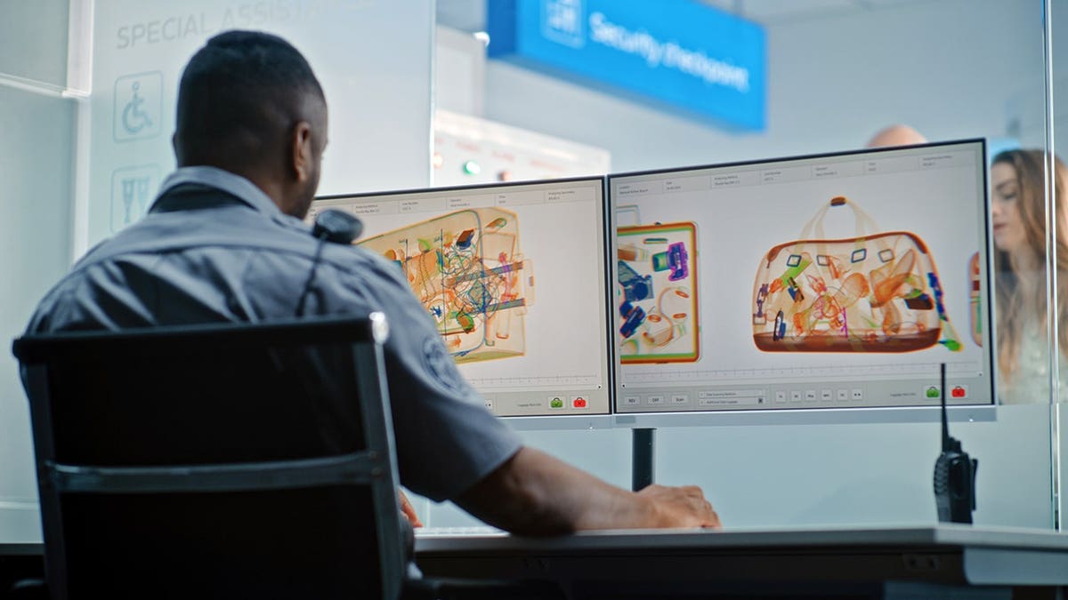 TSA worker monitors X-ray baggage screening at airport security checkpoint.