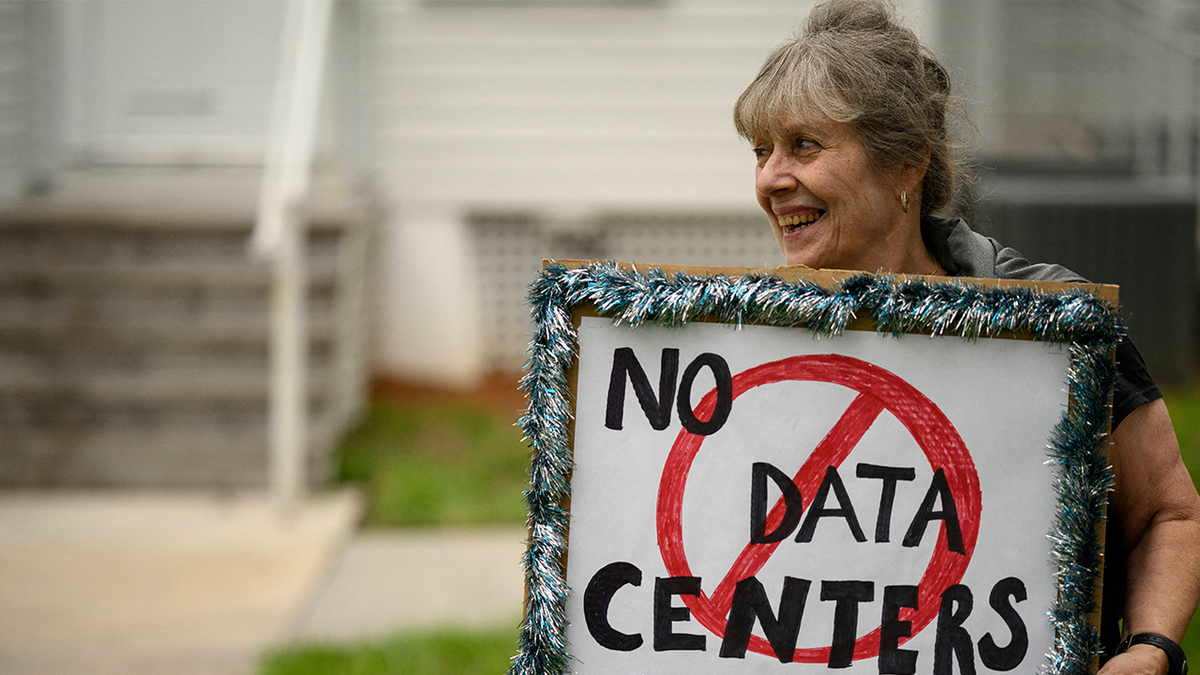 A woman holding signs outdoors during a protest against AI data center expansion.