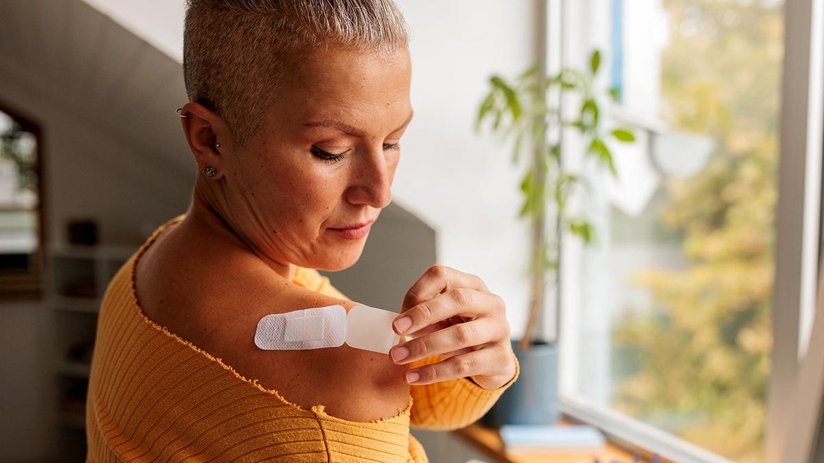 Woman applies a hormone replacement therapy patch to her shoulder at home.