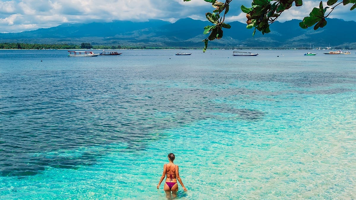 Woman in bikini relaxes in blue ocean water on a tropical island.