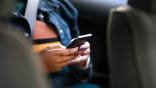 A woman looks at her phone in the backseat of a car.