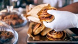 A gloved hand holds a cinnamon roll as it's being placed into a bag.