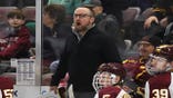 Greg Powers stands behind the bench during a college hockey game.