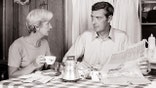 A couple have coffee at the kitchen table, as shown in black and white.
