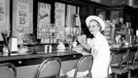 A woman sits at a lunch counter in the 1950s.