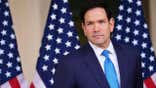 marco rubio stands before an american flag