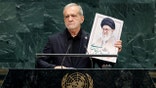 Masoud Pezeshkian holds an image of Ali Khamenei as he speaks from a podium.