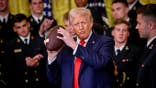 President Donald Trump holds up a football with Navy Midshipmen co-captain Colin Ramos in the East Room of the White House.