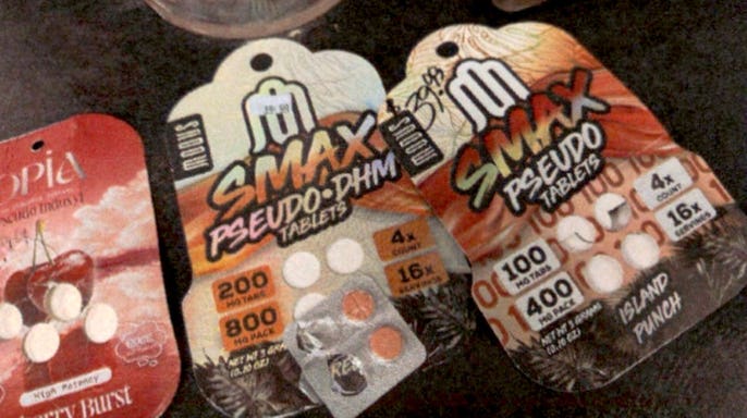 Three synthetic kratom tablet packages laid on a dark surface, including two Smax-brand packs and a cherry-flavored package, with loose tablets visible inside the blister packing.