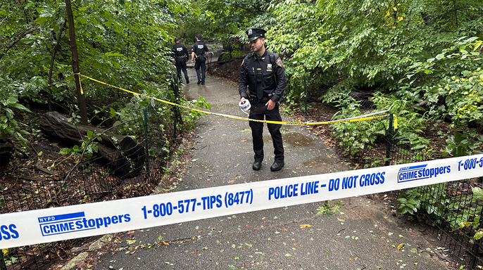 NYPD officers stand behind police tape on a wooded Central Park path