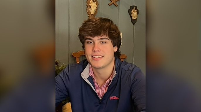Robert Strang in an Ole Miss pullover poses for ap ortrait in front of a green wall