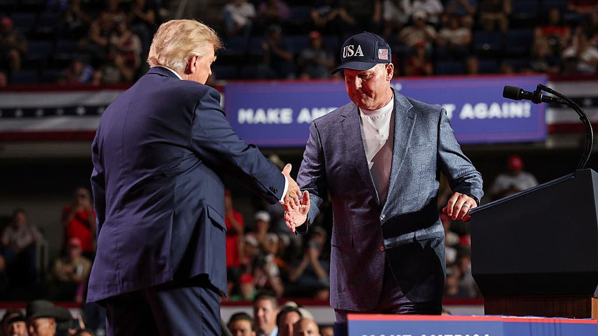 Donald Trump shakes hands with Roger Clemens on stage at a campaign rally