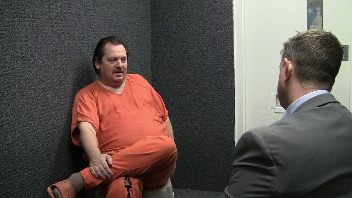 Aubrey Trail, vestido de naranja, siendo interrogado por la policía.