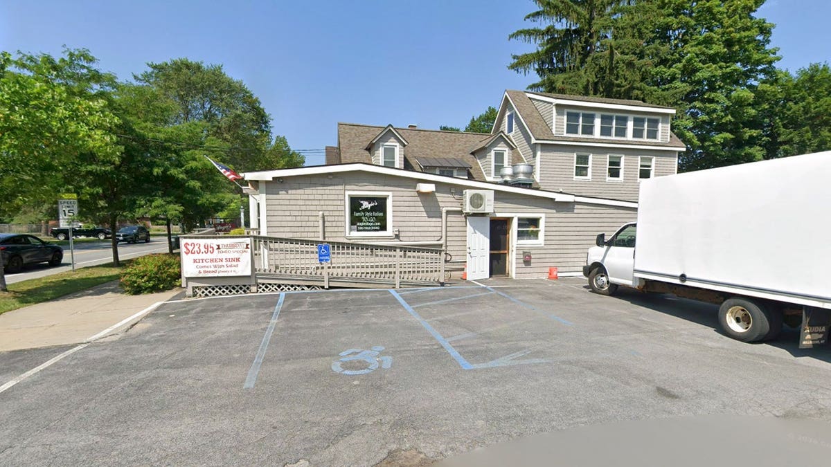 Exterior of a gray-shingled building with a wheelchair ramp, a sign advertising a $23.95 Thursday to-go special, and a white box truck parked beside an empty lot.