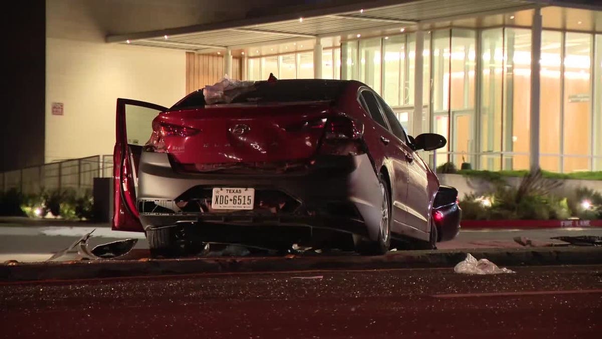A red Hyundai with extensive rear-end damage and an open driver's door sits near a building at night following a crash in Dallas.