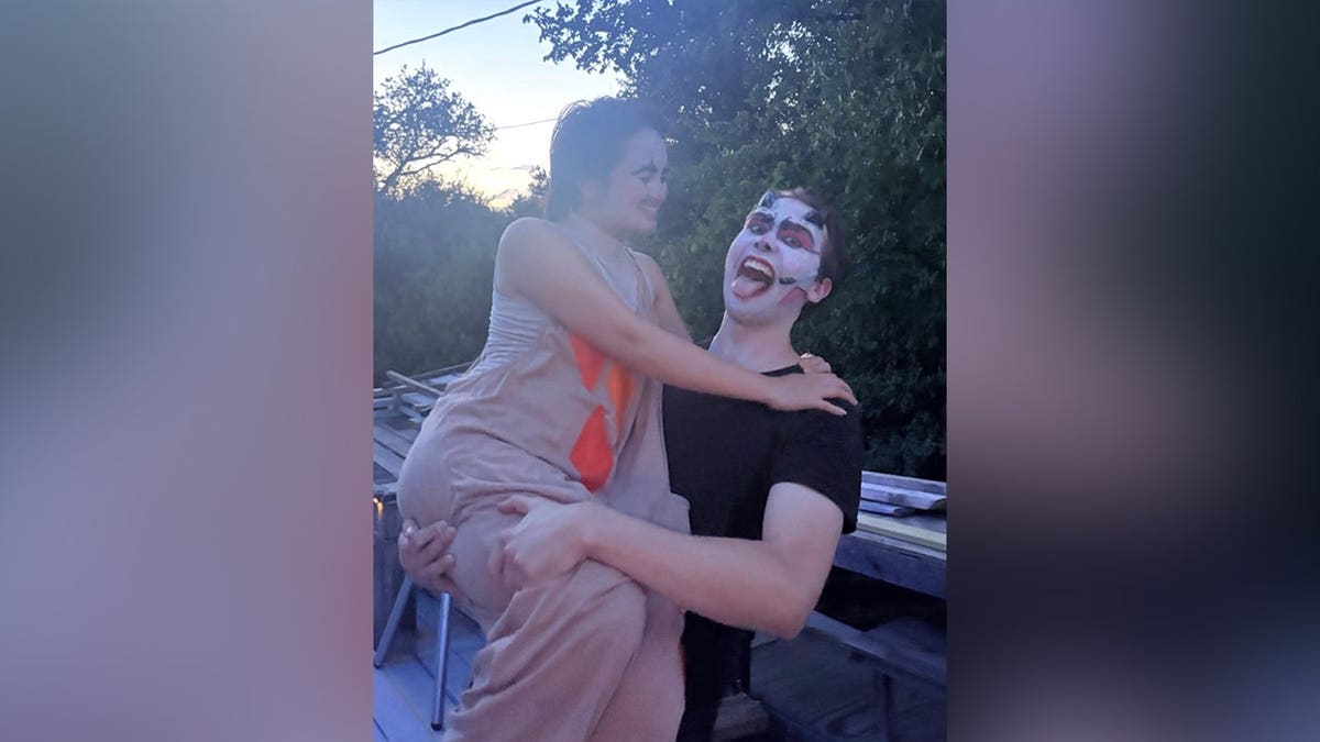 Julian Harris, wearing theatrical face makeup, holds Madison Duren in his arms as the couple smiles and poses outdoors.