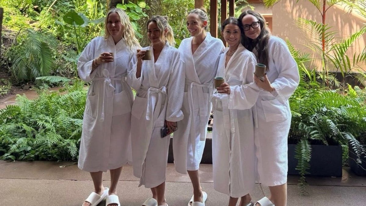 Hilary Duff poses with four friends wearing white spa robes beneath palm trees at a luxury resort in Mexico.