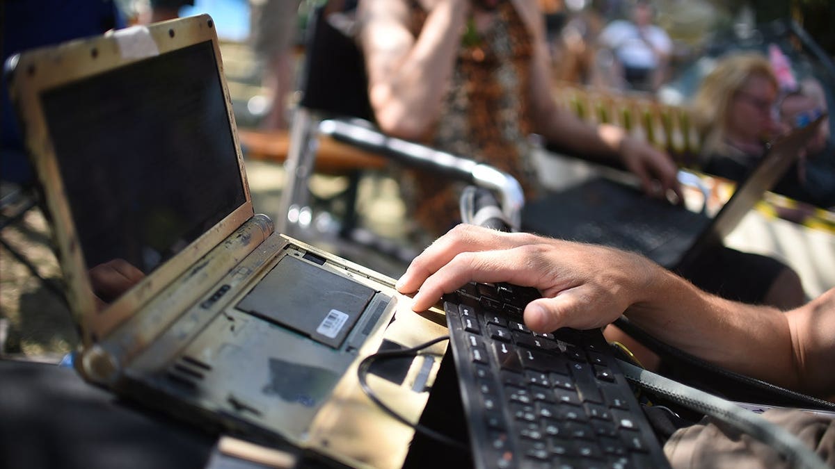 Hacker typing on a disassembled laptop.