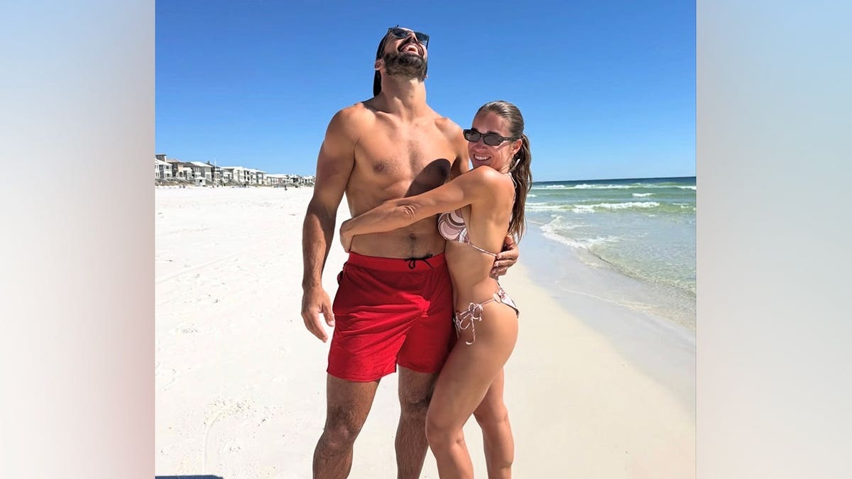 Jessie James Decker smiles in a patterned bikini and sunglasses while embracing her shirtless husband, Eric Decker, on a Florida beach.