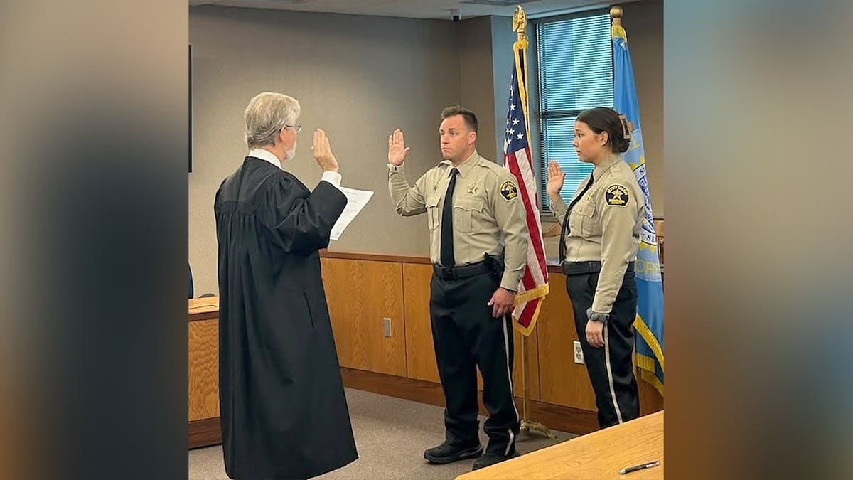 A judge in a black robe administers the oath of office to two Minnehaha County sheriff's deputies, including Katherine Frank, standing with their right hands raised.