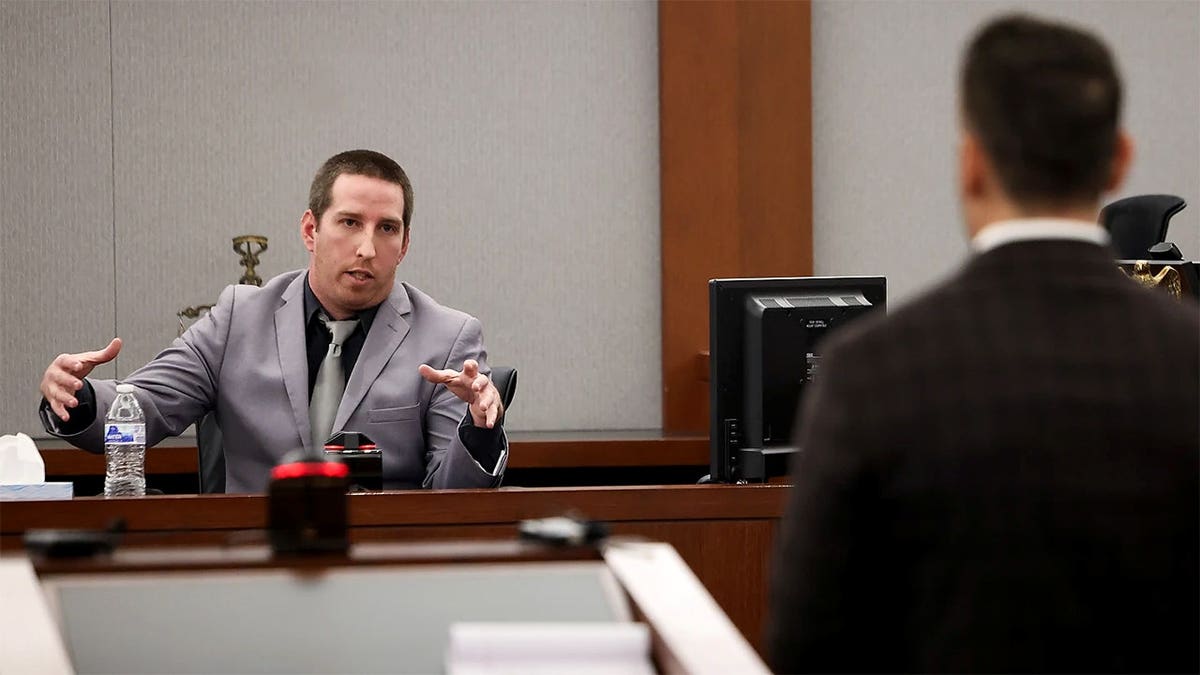 Mitchell Fairbarn, wearing a gray suit and tie, gestures with both hands while testifying in a Las Vegas courtroom.