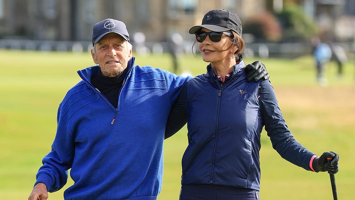 Catherine Zeta Jones and Michael Douglas stand on a golf course at St. Andrews.