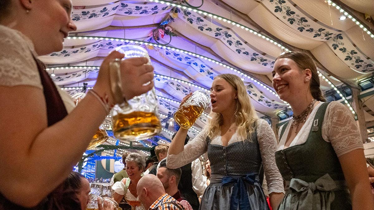 Kaya, Christina and Marlene stand on beer benches at Oktoberfest in Munich.