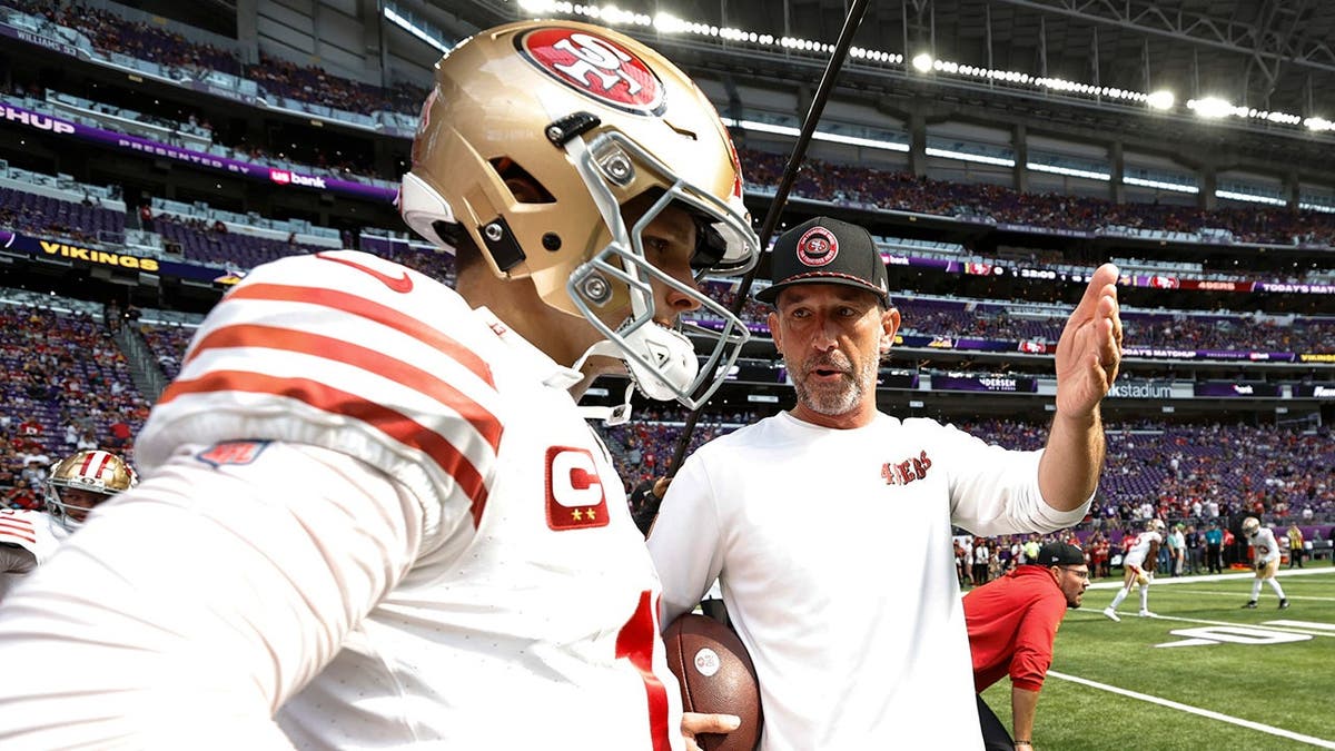 Brock Purdy and Kyle Shanahan stand before a game at U.S. Bank Stadium in Minneapolis.