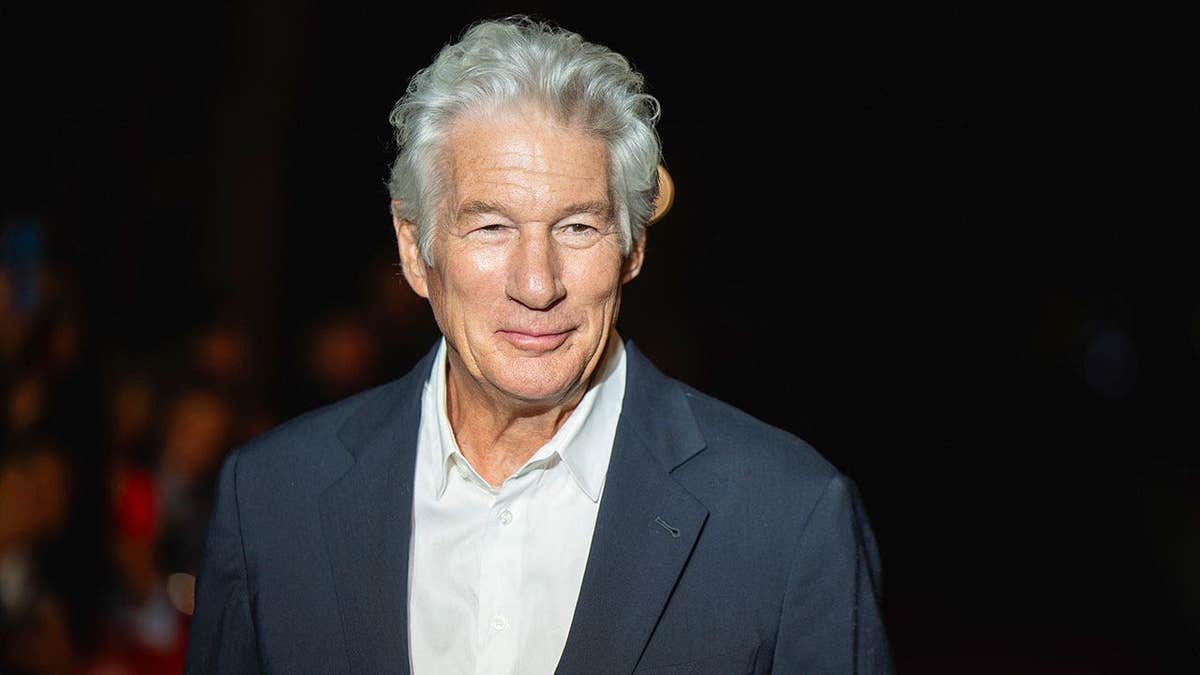Richard Gere wearing a grey suit and a white shirt on the red carpet.